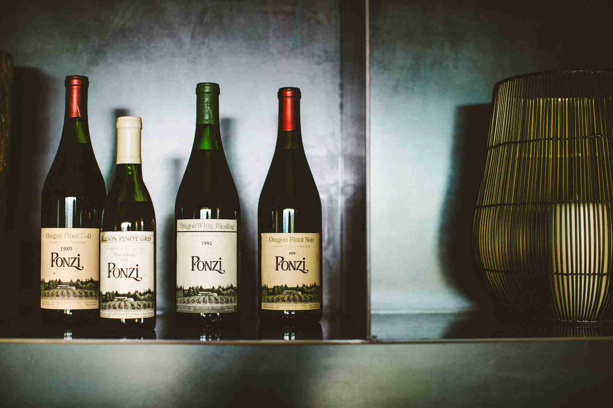 Four Ponzi wine bottles on a shelf with a decorative lamp in the background.