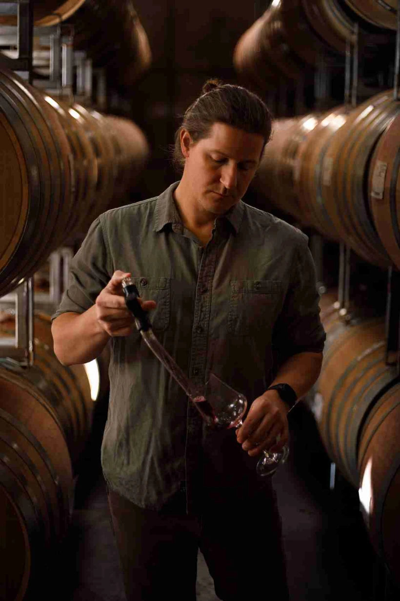 Person sampling wine from a barrel in a winery